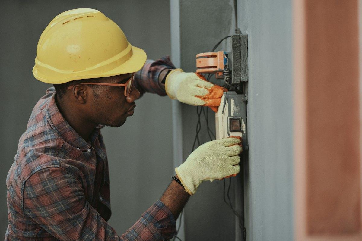 Technician in a hard hat testing an electrical panel